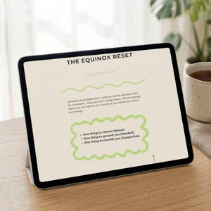 May include: A digital tablet displaying a wellness guide titled "THE EQUINOX RESET." The screen features text about balancing life and includes prompts to release, ground, and nourish. The tablet rests on a wooden surface, with a mug visible in the background.