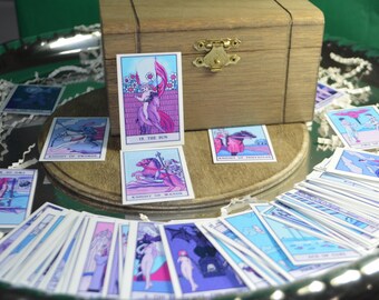 May include: A wooden box with a hinged lid and a metal latch. The box is open and contains a deck of tarot cards. The cards are arranged in a fan shape and feature colorful illustrations. The cards include "The Sun", "Knight of Wands", and "Knight of Pentacles".