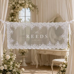 May include: A rectangular white lace banner featuring intricate floral embroidery along the edges. The center displays the text The REEDS and EST. 2026 in a white serif font. The banner is suspended by white ribbons on both sides.