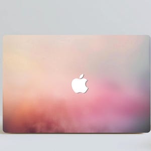 May include: A laptop featuring a vibrant gradient design in pink, orange, and purple hues. The Apple logo is visible in white on the laptop's surface. The laptop is placed on a white surface.