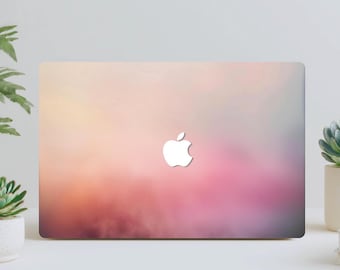 May include: A laptop with a colorful gradient design in shades of pink, orange, and purple. The Apple logo is prominently displayed in white on the laptop's surface. The laptop is on a white surface.