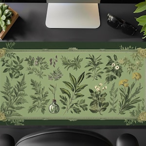 Puede incluir: Una alfombrilla de escritorio verde con una ilustración botánica vintage de varias plantas y flores. La ilustración está enmarcada con un borde dorado y se coloca sobre un fondo verde oscuro.
