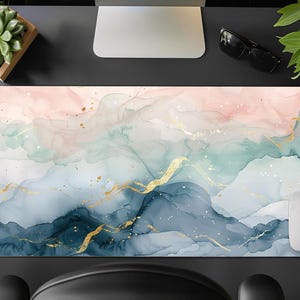 May include: Abstract desk mat with a watercolour design in shades of pink, blue, and green with gold accents. The mat is designed to protect your desk surface and add a touch of style to your workspace.