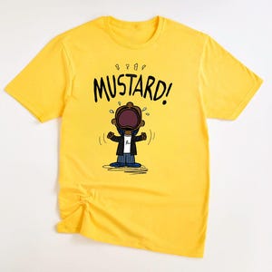May include: A yellow t-shirt with a cartoon character wearing a black jacket and blue jeans. The character is crying and the text "MUSTARD!" is above the character.
