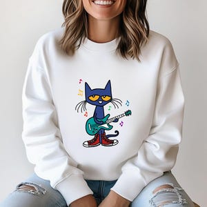 May include: White sweatshirt with a blue cat playing a green electric guitar. The cat has yellow eyes and is wearing red sneakers. There are rainbow colored musical notes around the cat.
