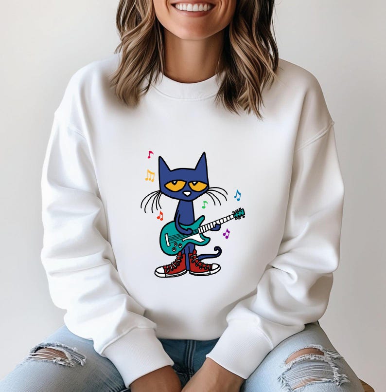 May include: White sweatshirt with a blue cat playing a green electric guitar. The cat has yellow eyes and is wearing red sneakers. There are rainbow colored musical notes around the cat.