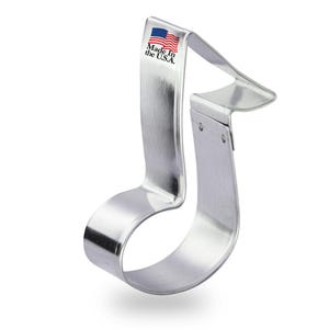 May include: Silver metal cookie cutter shaped like a treble clef. The cutter has a "Made in the U.S.A." label on the top.