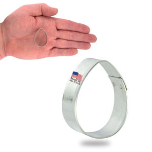 May include: A silver metal cookie cutter shaped like a teardrop. The cookie cutter is made in the USA.