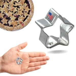 May include: A silver star-shaped cookie cutter with a "Made in the U.S.A." label. The cutter is shown next to a hand holding a smaller version of the cutter.