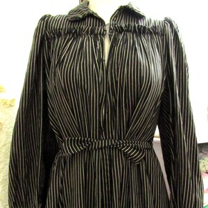 May include: Black and white striped dress with long sleeves. The dress features a collared neckline, a cinched waist with a tie, and button details down the front. The vertical stripes create a slimming effect.