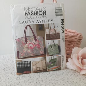 May include: A McCall's Fashion Accessories sewing pattern featuring Laura Ashley designs. The pattern packet displays images of various tote bags, including one with a floral print and another with a plaid design. The pattern number is M4531.