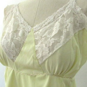 May include: A pale yellow slip with white lace detailing. The slip features a V-neck design with delicate lace trim along the neckline and straps. The bodice is accented with a decorative trim at the waist, creating a vintage aesthetic.