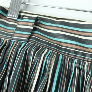 May include: A black, brown, and teal striped skirt with pleats. The skirt has a waistband with a button closure.
