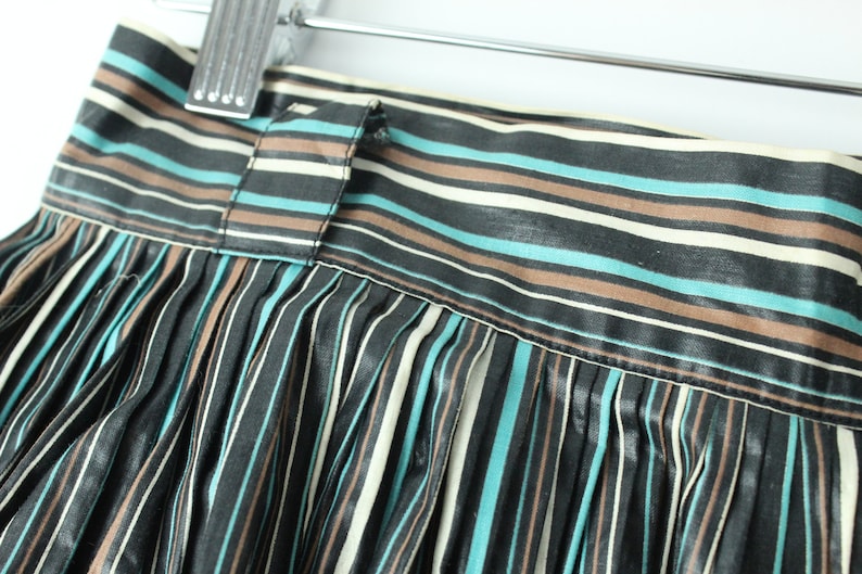 May include: A black, brown, and teal striped skirt with pleats. The skirt has a waistband with a button closure.