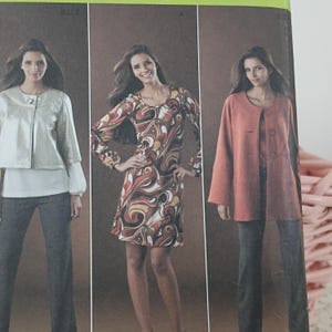 May include: A fashion magazine cover featuring three women modeling different outfits. The first model wears a silver jacket over a white top and dark pants. The second model is in a patterned dress. The third model wears a coral jacket and dark pants.