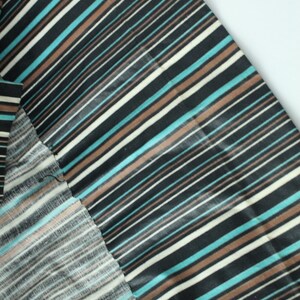 May include: Close-up of a black and white striped fabric with brown and blue stripes. The fabric is folded over itself, showing the different sides of the fabric.