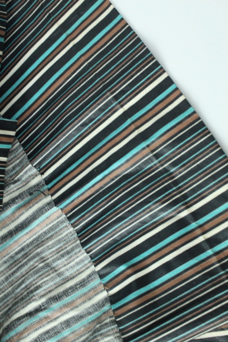 May include: Close-up of a black and white striped fabric with brown and blue stripes. The fabric is folded over itself, showing the different sides of the fabric.