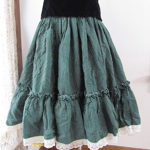 May include: A vintage dress featuring a black velvet bodice and a green skirt with white polka dots. The skirt has multiple ruffled tiers and is trimmed with white lace. The dress is displayed on a white mannequin.