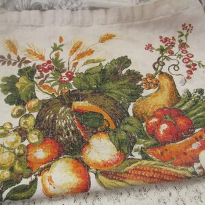 May include: A vintage linen kitchen towel with a colorful autumn harvest print. The design features a variety of fruits and vegetables, including grapes, pumpkins, gourds, tomatoes, corn, and watermelon.