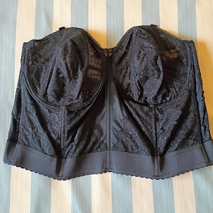 May include: A black, strapless bustier with a floral lace overlay. The bustier has molded cups and a smooth, satin-like panel down the center. The bottom edge features a scalloped trim.