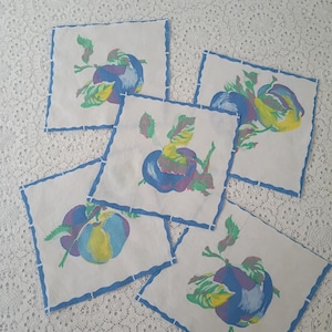 May include: Set of five square white fabric napkins. Each napkin features a colorful illustration of a fruit with blue, purple, yellow, and green hues. The edges are trimmed with a blue zigzag border.