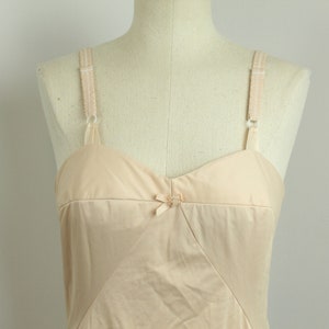 May include: A beige slip with adjustable straps and a bow detail at the center of the bust.