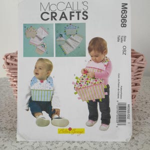 May include: McCall's Crafts sewing pattern M6368 featuring baby bibs. The pattern includes illustrations of bibs with cupcake designs, in various colors. The pattern also includes the Cotton Ginny's logo.