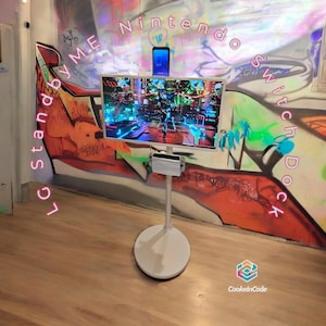 May include: A white stand with a round base, holding a TV screen displaying a video game. The stand is labelled "LG stand by ME" in pink lettering. The wall behind the stand is painted with colourful graffiti, including the words "Nintendo Switch Dock" in pink lettering.
