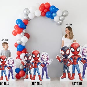 May include: A party decoration set featuring Spider-Man character cutouts, ranging from 30 to 45 inches tall, with a balloon arch. The arch is composed of red, white, silver, and blue balloons. A woman and a child are visible in the background.