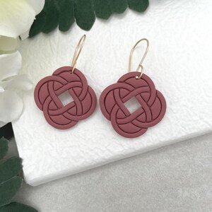 May include: A pair of burgundy red polymer clay earrings with a knotted design. The earrings have gold hooks.