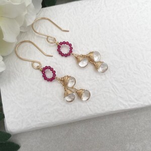 May include: Gold earrings with a circle of pink beads and two clear teardrop-shaped stones hanging from each earring.