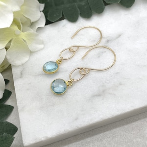 May include: A pair of gold dangle earrings with light blue gemstone drops. The earrings have a simple, elegant design.