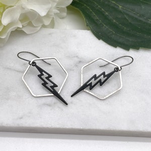 Può includere: Un paio di orecchini esagonali in argento con un design a forma di fulmine nero. Gli orecchini hanno uno stile semplice e moderno.