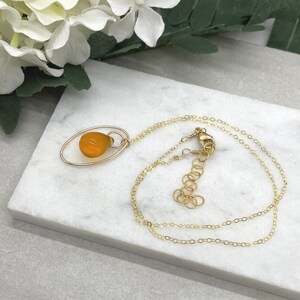 May include: A gold chain necklace with a pendant featuring a teardrop-shaped amber stone set in a gold oval frame.