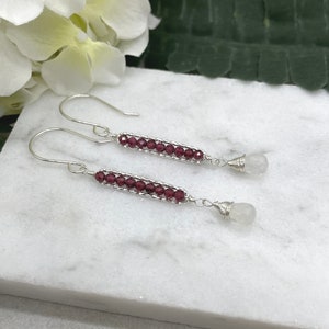 May include: A pair of silver dangle earrings with a row of small, dark red garnet beads and a white moonstone drop at the end of each earring.
