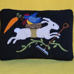May include: A black pillow with a white rabbit carrying a bird's nest with two birds. The rabbit is holding a rake and there is a carrot in the background.