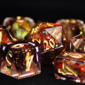 May include: Set of seven polyhedral dice with a reddish-brown and gold glitter design. The dice have gold numbers and are made of a clear resin. The dice are for tabletop games.