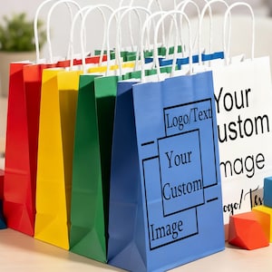 May include: A collection of colorful paper gift bags with white handles. The bags are in red, yellow, green, blue, and white. The blue and white bags have text that reads "Logo/Text", "Your Custom Image". Colorful wooden blocks are in the foreground.
