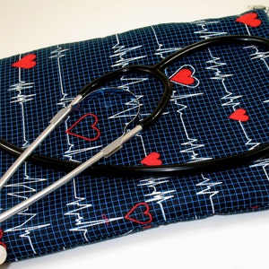 May include: A black stethoscope with a silver chrome finish is lying on top of a blue fabric pouch with a white EKG pattern and red hearts.