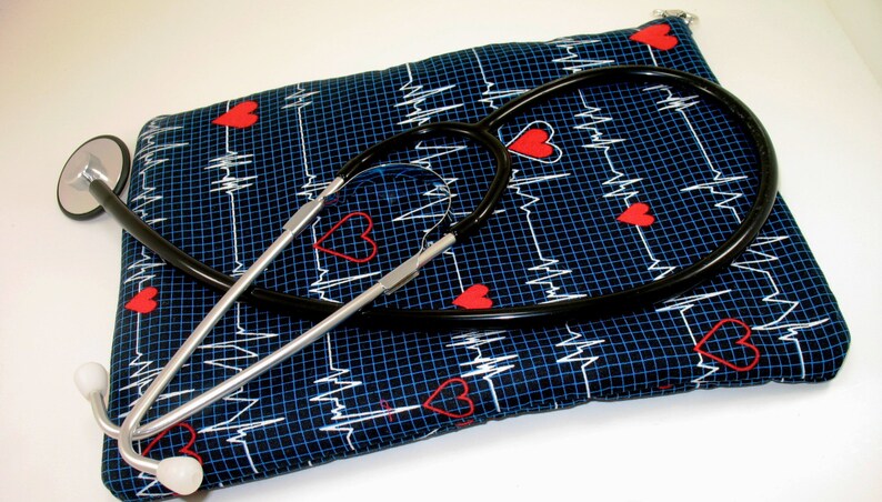 May include: A black stethoscope with a silver chrome finish is lying on top of a blue fabric pouch with a white EKG pattern and red hearts.