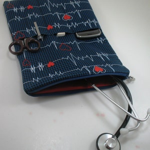 May include: A blue zippered pouch with a red lining and a white and red EKG pattern. The pouch is open and a stethoscope is partially inside. The pouch has multiple pockets and a cell phone is visible in one of the pockets.