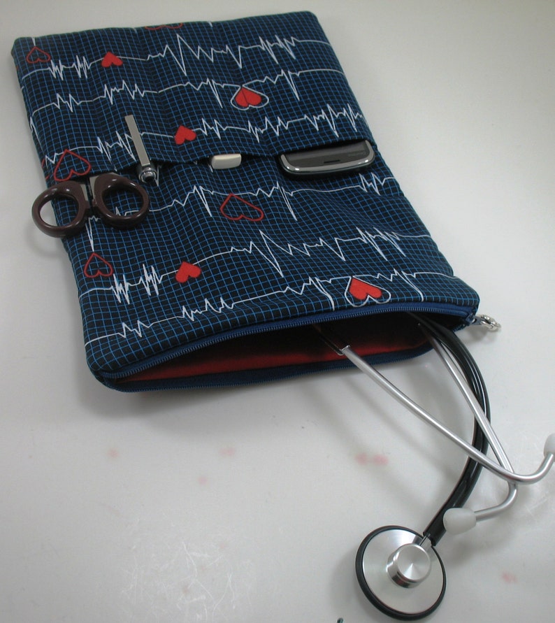 May include: A blue zippered pouch with a red lining and a white and red EKG pattern. The pouch is open and a stethoscope is partially inside. The pouch has multiple pockets and a cell phone is visible in one of the pockets.