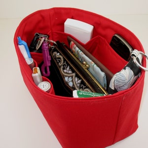 May include: Red fabric organizer with multiple compartments for a purse or handbag. The organizer is filled with various items, including a phone, wallet, keys, and a small bottle of hand sanitizer.