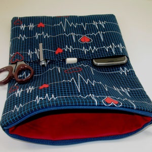 May include: A blue zippered pouch with a red lining. The pouch has a repeating pattern of white heartbeats and red hearts on a blue background. The pouch has a pocket on the front that can hold a phone or other small items.