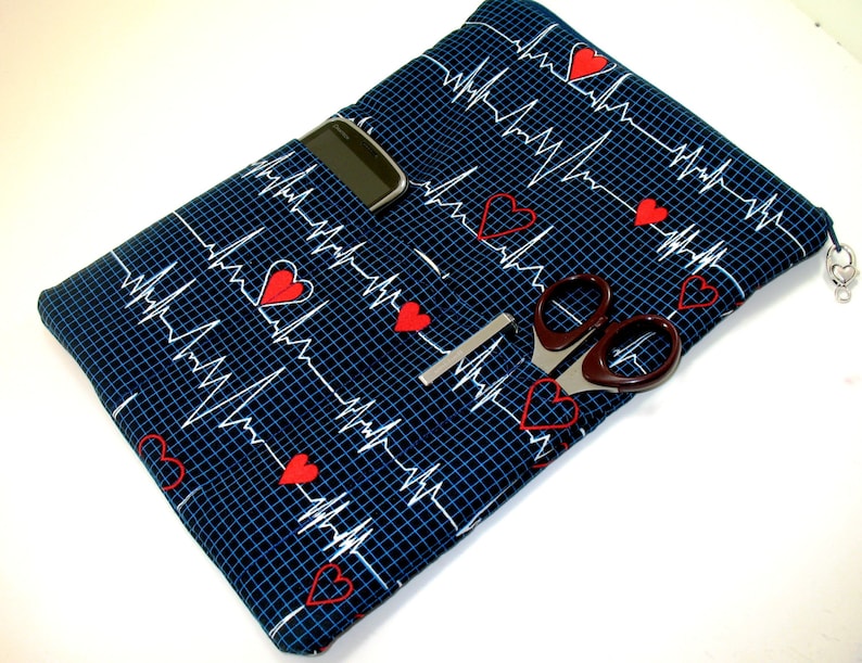 May include: A blue fabric pouch with a repeating pattern of red hearts and white EKG lines. The pouch has a zipper closure and a small pocket on the front. It also has a silver chain attached to the zipper pull.