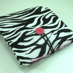 May include: A black and white zebra print fabric pouch with a pink button closure. The pouch is closed and has a black strap.