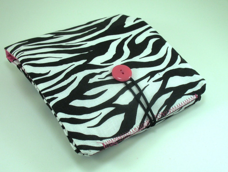 May include: A black and white zebra print fabric pouch with a pink button closure. The pouch is closed and has a black strap.