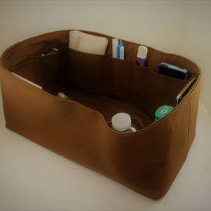 Op de afbeelding: Een bruine felt handtas organizer met meerdere vakken en compartimenten. De organizer is gevuld met verschillende items, waaronder pennen, een telefoon en een waterfles.
