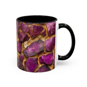 May include: A white ceramic coffee mug with a black interior and handle. The exterior features a mosaic design of purple and gold-colored stones. The mug is designed for hot or cold beverages.