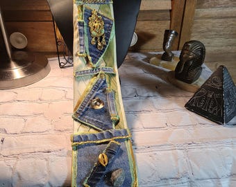 May include: A beige tie with a green beaded necklace. The tie is decorated with denim patches, gold accents, and various embellishments.
